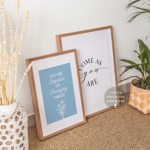 May include: Two framed prints with inspirational quotes. The print on the left says "You are capable of amazing things" in white text on a light blue background. The print on the right says "Come as you are" in black cursive text on a white background.