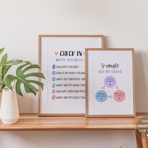May include: Two printable posters with a light wood frame. The poster on the left has a pink heart and the text "Check in with yourself" with a list of questions. The poster on the right has the text "Triangle Deep Breathing" with a diagram of a triangle with instructions for deep breathing.