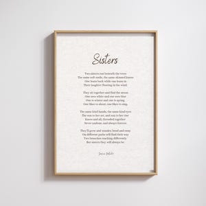 May include: A framed print with the word "Sisters" at the top, followed by a poem about sisterhood. The print has a light beige background and a wooden frame. The poem is written in a classic, elegant font.