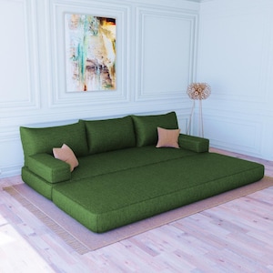 Könnte beinhalten: Ein dunkelgrünes modulares Sofa mit drei Kissen und einem hellbraunen Kissen. Das Sofa steht in einem Raum mit weißen Wänden und einem Holzboden.