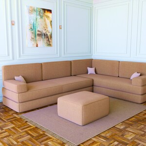 May include: A brown sectional sofa with a matching ottoman in a living room setting. The sofa has two cushions on each side and a single cushion on the back. The ottoman is square and has a smooth surface.