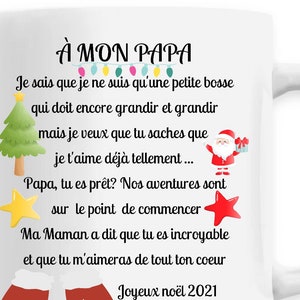 Peut inclure: Mug en céramique blanche avec un motif sur le thème de Noël. Le mug représente un Père Noël rouge et blanc, une étoile rouge, une étoile jaune et une moufle rouge et blanche. Le texte sur le mug est "À MON PAPA" et comprend un message sur l'amour d'un enfant pour son père. Le texte comprend également l'année "2021".