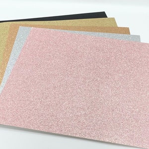 May include: A stack of four glitter paper sheets in black, gold, silver, and pink.