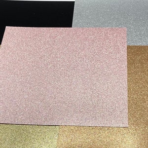 May include: Five sheets of glitter paper in different colors: black, pink, silver, gold, and bronze. The sheets are arranged in a stack, with the black sheet on the bottom and the bronze sheet on the top.