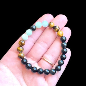 Op de afbeelding: Een armband met zwarte, bruine en groene kralen. De armband is gemaakt van natuurlijke stenen.