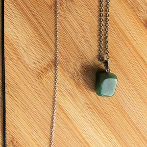 Op de afbeelding: Twee kettingen op een houten oppervlak. De ene ketting heeft een zwart koord en de andere een zilveren ketting. De zilveren ketting heeft een groene stenen hanger.
