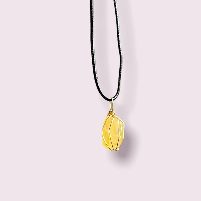 May include: A yellow crystal pendant wrapped in gold wire, hanging from a black cord necklace.
