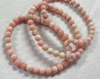 May include: Three pink beaded bracelets. Each bracelet is made of small, round, light pink beads. The bracelets are arranged in a slightly overlapping pattern, showcasing their delicate design and color.