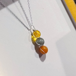 May include: A silver chain necklace with three round beads. The beads are yellow, gray, and orange.