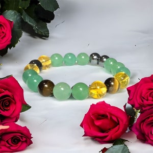 May include: A green, yellow, and brown beaded bracelet with a silver bead. The bracelet is surrounded by red roses.