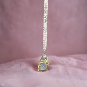 May include: A silver chain necklace with a raw opal pendant wrapped in silver wire. The opal is iridescent with shades of blue, green, and purple.