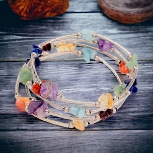 May include: A multi-strand wrap bracelet featuring silver-toned metal wire and small, irregular, polished gemstone chips in various colors including purple, blue, green, orange, and yellow, interspersed with small silver-toned metal beads.