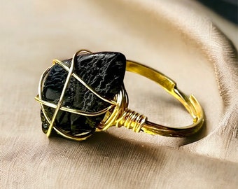 Puede incluir: Un anillo de alambre dorado con una piedra preciosa negra. El anillo está colocado sobre un fondo de tela beige.