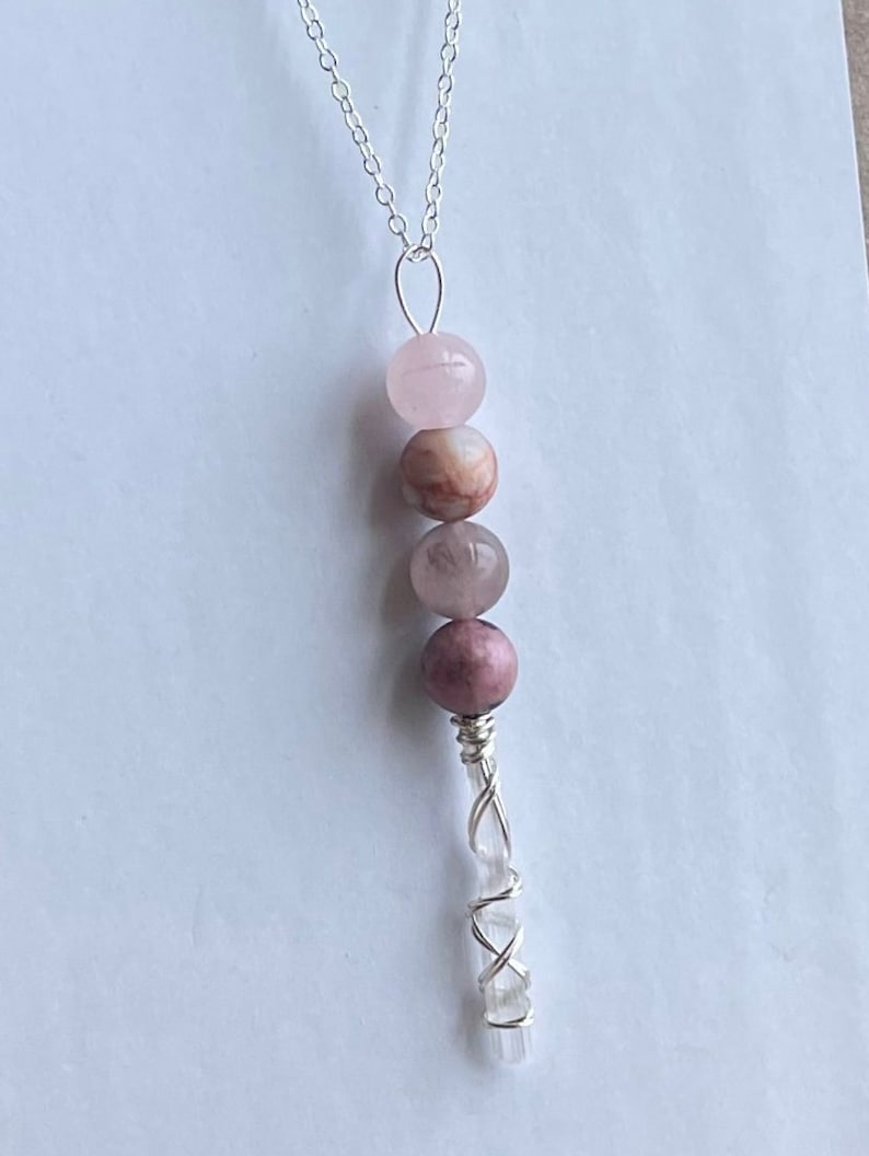 May include: A silver chain necklace with a pink and white crystal pendant. The pendant features a clear crystal wrapped in silver wire and three pink and white gemstone beads.