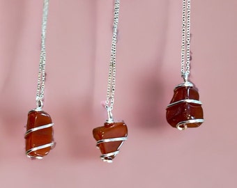 May include: Three silver necklaces with carnelian stone pendants. Each pendant is wrapped in silver wire.