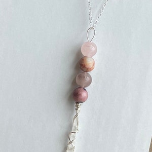 May include: A silver chain necklace with a crystal point pendant wrapped in silver wire. The pendant is adorned with four pink and brown gemstone beads.