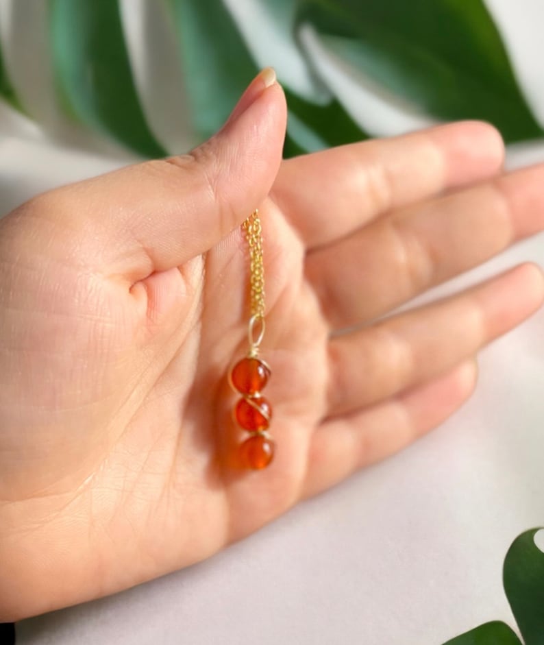 Pode incluir: Um colar de corrente de ouro com um pingente feito de tr&ecirc;s contas de cornalina envoltas em fio de ouro.