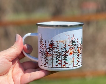 May include: White enamel mug with a colorful watercolor design of a forest. The trees are in shades of red, orange, yellow, green, and blue.