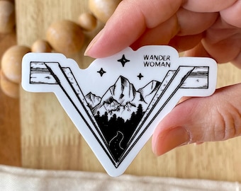 May include: Black and white sticker with a mountain range design and the text "Wander Woman" in a white rectangle. The sticker is on a white background.