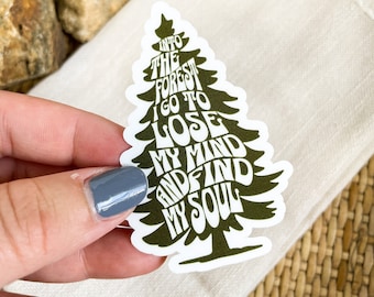 May include: A die-cut sticker shaped like a pine tree with a white border. The sticker features dark olive green text that reads INTO THE FOREST I GO TO LOSE MY MIND AND FIND MY SOUL, with the letters forming the silhouette of the tree.