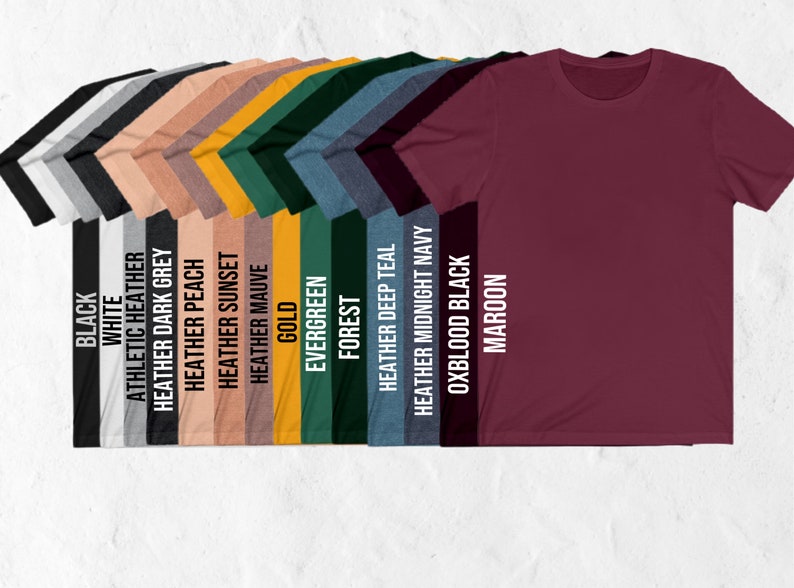 May include: A selection of t-shirts in various colors, including black, white, heather grey, heather peach, heather sunset, heather mauve, gold, evergreen, forest, heather deep teal, heather midnight navy, oxblood black, and maroon.