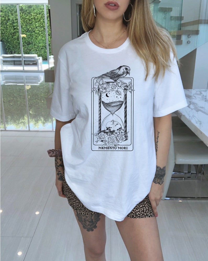 May include: White t-shirt with a black and white graphic of an hourglass, flowers, a bird, and the text "Memento Mori".