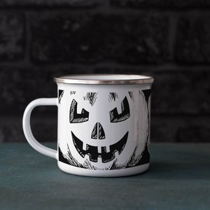 May include: White enamel mug with a black and white illustration of a jack-o'-lantern face.