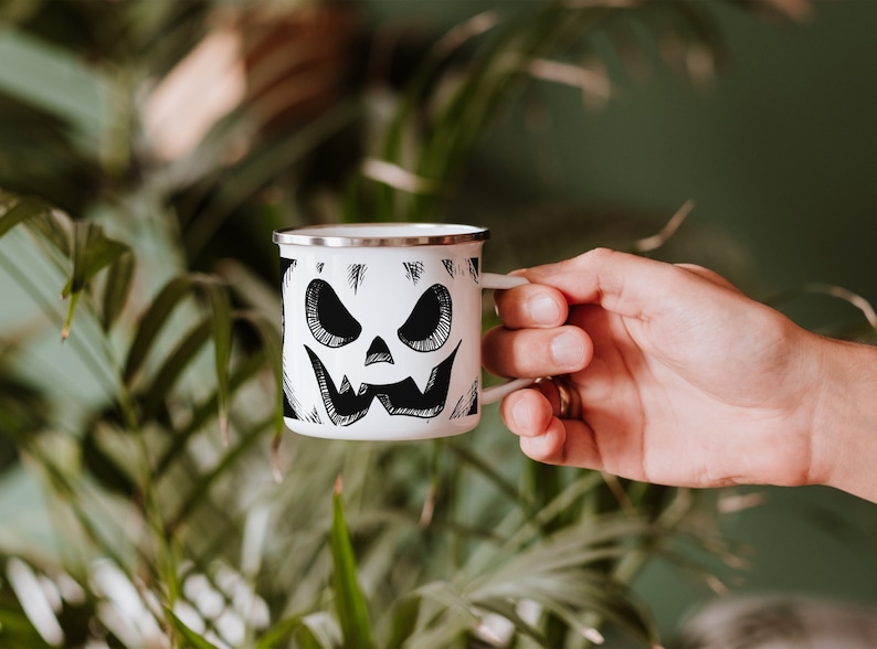 May include: White enamel camping mug with a black and white illustration of a jack-o'-lantern face.