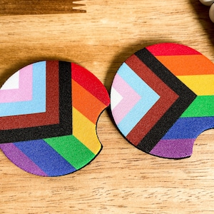 May include: Two round, colorful coasters with a geometric design featuring a rainbow and a transgender pride flag. The coasters are made of a soft, absorbent material and are perfect for protecting surfaces from spills.