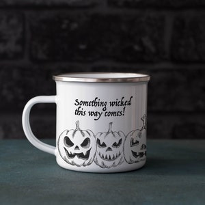 May include: White enamel camping mug with a black and white illustration of jack-o'-lanterns and the text "Something wicked this way comes!"
