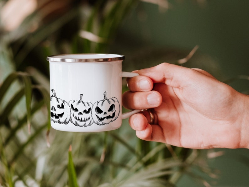 May include: White enamel mug with a black and white illustration of three jack-o'-lantern faces.