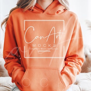 Könnte beinhalten: Ein leuchtend orangefarbener Hoodie mit einem weißen Kordelzug und einem weißen Logo, das "Can Art Mocks" mit dem Slogan "Creativity Meets Perfection" lautet.