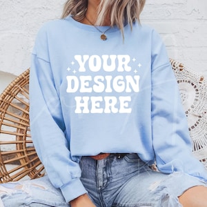 Op de afbeelding: Een lichtblauw sweatshirt met de tekst "YOUR DESIGN HERE" in wit. Het sweatshirt heeft lange mouwen en een ontspannen pasvorm.