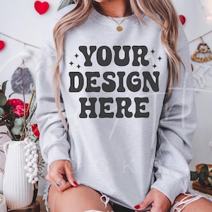 May include: A gray sweatshirt with the text "YOUR DESIGN HERE" in black letters. The sweatshirt is being worn by a person with long brown hair.