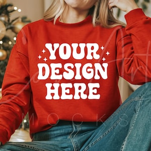 May include: A red sweatshirt with the text "YOUR DESIGN HERE" in white. The sweatshirt is being worn by a person sitting down.