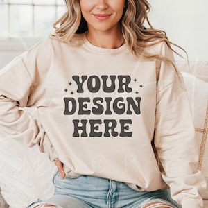 Puede incluir: Una sudadera beige de manga larga y cuello redondo. La sudadera tiene el texto "YOUR DESIGN HERE" impreso en la parte delantera en una fuente retro.