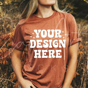 May include: A rust-colored t-shirt with the text "YOUR DESIGN HERE" in white. The shirt is worn by a person standing in a field of tall grass.
