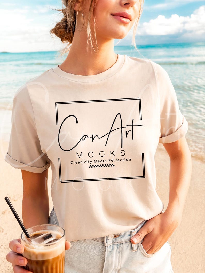May include: A woman wearing a beige t-shirt with the text "Can Art Mocks Creativity Meets Perfection" printed on it. She is standing on a beach and holding a glass of iced coffee.