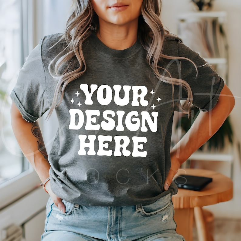 K&ouml;nnte beinhalten: Dunkelgraues T-Shirt mit dem wei&szlig;en Text "YOUR DESIGN HERE" in Retro-Schrift. Das Rundhals-Shirt hat hochgekrempelte &Auml;rmel. Das Model tr&auml;gt eine blaue Jeans.
