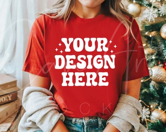 Könnte beinhalten: Ein rotes T-Shirt mit dem Text "YOUR DESIGN HERE" in Weiß. Das Shirt wird von einer Person vor einem Weihnachtsbaum getragen.