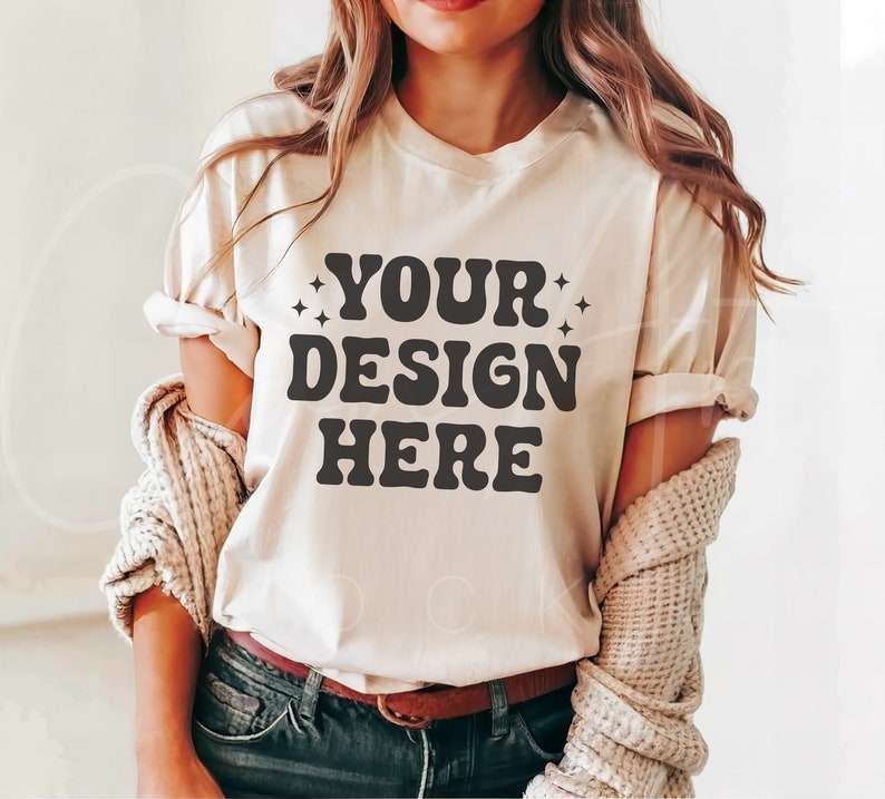 Peut inclure: Un t-shirt blanc avec le texte "YOUR DESIGN HERE" en lettres noires de style r&eacute;tro.