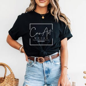 Pode incluir: Uma camiseta preta com um design gr&aacute;fico branco que diz "CanArt Mocks" e "Creativity Meets Perfection". A camiseta est&aacute; amarrada na frente e usada com um cinto marrom e shorts jeans azuis.