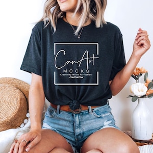 Pode incluir: Uma mulher vestindo uma camiseta cinza escura com o texto "Can Art Mocks Creativity Meets Perfection" em um quadrado branco. Ela est&aacute; vestindo shorts jeans azuis e tem o cabelo puxado para tr&aacute;s.