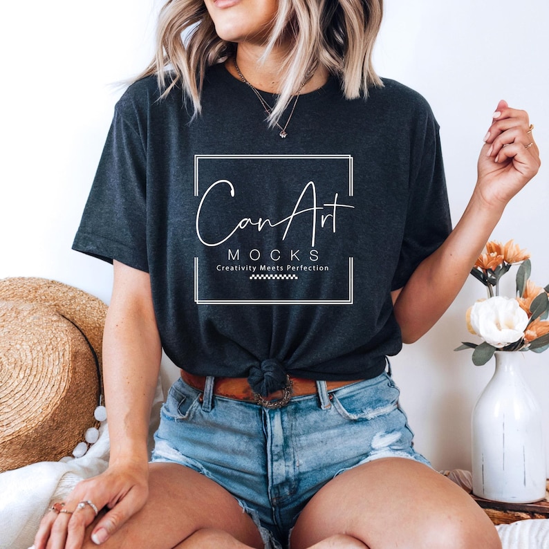 Pode incluir: Uma mulher vestindo uma camiseta cinza escura com o texto "Can Art Mocks Creativity Meets Perfection" em um quadrado branco. Ela est&aacute; vestindo shorts jeans azuis e tem o cabelo puxado para tr&aacute;s.