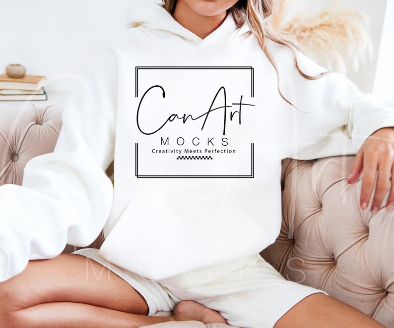 The image shows a woman in a plain white hoodie on a beige couch. The outfit is simple and comfortable. The bright background makes it ideal for everyday wear.