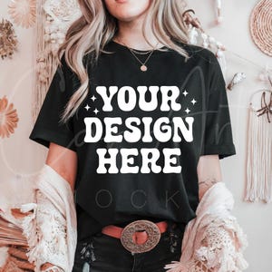 May include: A black t-shirt with the text "YOUR DESIGN HERE" in white. The shirt is being worn by a person with long blonde hair.