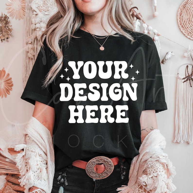 May include: A black t-shirt with the text "YOUR DESIGN HERE" in white. The shirt is being worn by a person with long blonde hair.