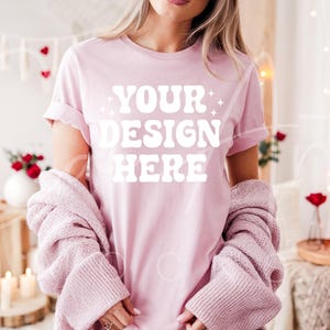 May include: A pink t-shirt with the text "YOUR DESIGN HERE" in white. The shirt is being worn by a person with long brown hair. The person is wearing a pink cardigan over the shirt.