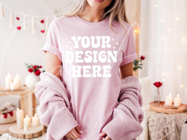 May include: A pink t-shirt with the text "YOUR DESIGN HERE" in white. The shirt is being worn by a person with long brown hair. The person is wearing a pink cardigan over the shirt.