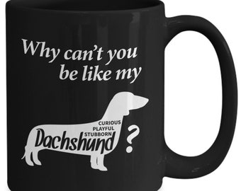 May include: Black coffee mug with white text that reads "Why can't you be like my Dachshund?" with a silhouette of a dachshund with the words "Curious, Playful, Stubborn" inside the silhouette.